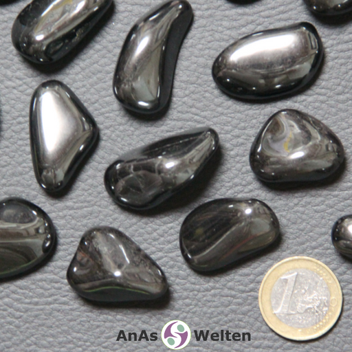 Das Bild zeigt einen Hämatit Trommelstein anhand von mehreren Beispielsteinen. Die Edelsteine haben allesamt eine dunkelgraue, spiegelnde Oberfläche, die metallen aussieht.