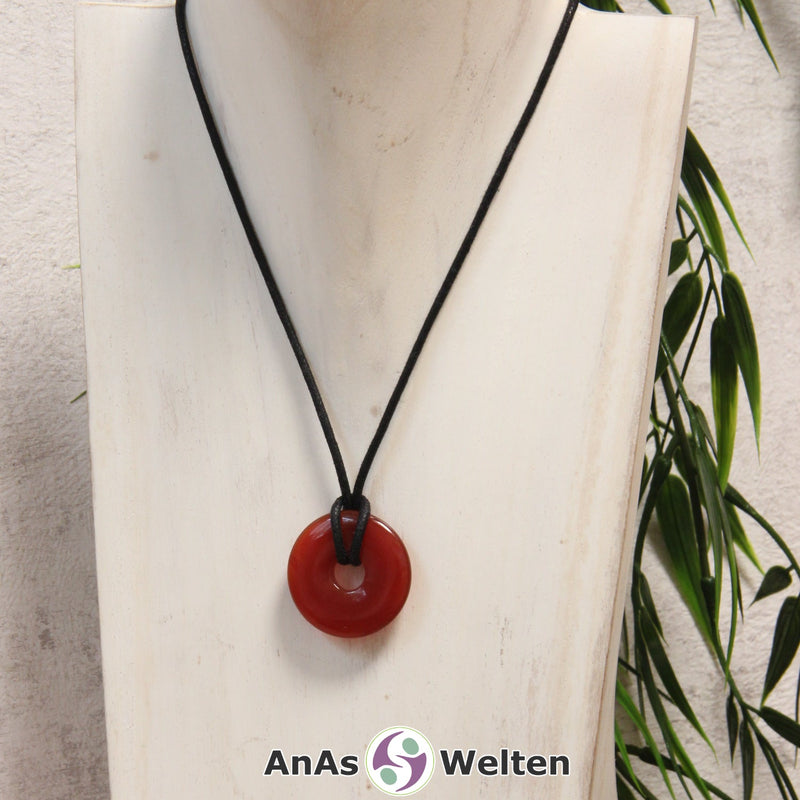 Ein Karneol Donut als Kette an einem schwarzen gewachsten Baumwollband um eine helle Büste.