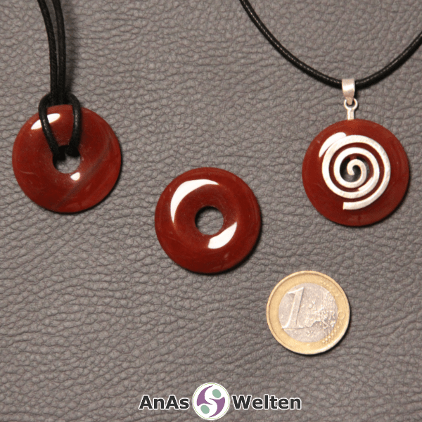 Drei Karneol Donuts nebeneinander. Einer an einem Baumwollband, ein anderer an einem Donut-Halter mit Baumwollband.