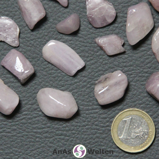 Das Bild zeigt einen Kunzit Trommelstein als mehrere Beispielsteine. Die Edelsteine haben allesamt eine zartrosa Farbe. Bei einigen Steinen sind gräuliche Einschlüsse und/oder weiße Risse im Inneren zu erkennen.