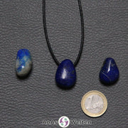 Drei blaue Lapislazuli gebohrte Trommelsteine nebeneinander. Einer befindet sich an einem schwarzen gewachsten Baumwollband.