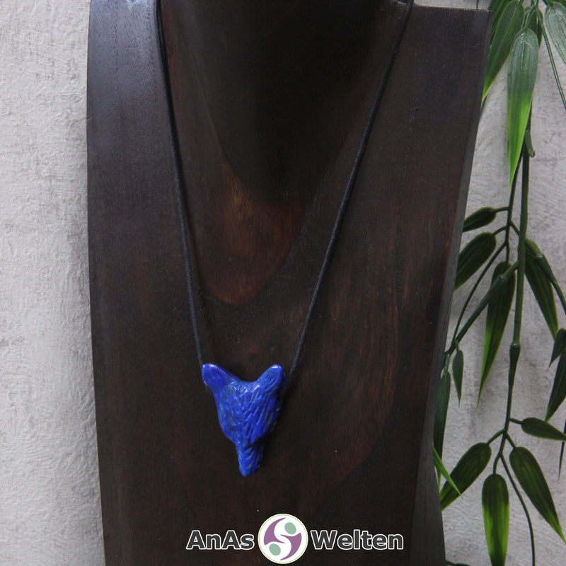 Ein Lapislazuli Wolf Anhänger an einem schwarzen Baumwollband, der um eine dunkle Büste gehängt wurde.