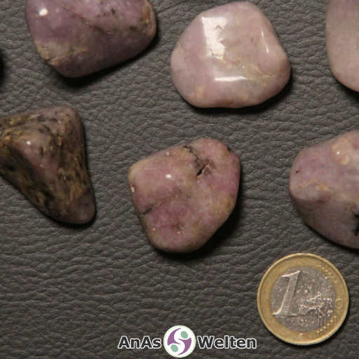 Das Bild zeigt einen Lepidolith Trommelstein anhand von mehreren Beispielsteinen. Die Edelsteine haben eine rosa-beige Farbe mit einem unregelmäßigen Muster. Einige von ihnen haben Einschlüsse in einem dunklen Braun.