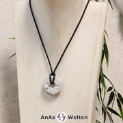 Ein Magnesit Donut als Kette an einem schwarzen gewachsten Baumwollband um eine helle Büste.