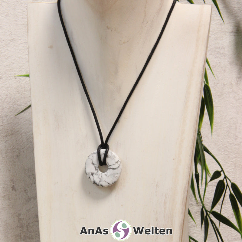 Ein Magnesit Donut als Kette an einem schwarzen gewachsten Baumwollband um eine helle Büste.