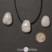 Drei weiße Magnesit gebohrte Trommelsteine nebeneinander. Einer befindet sich an einem schwarzen gewachsten Baumwollband.