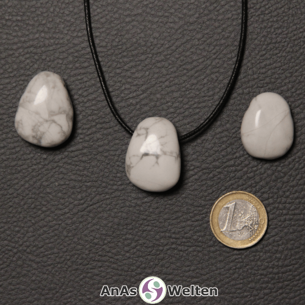 Drei weiße Magnesit gebohrte Trommelsteine nebeneinander. Einer befindet sich an einem schwarzen gewachsten Baumwollband.