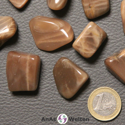 Das Produktbild zeigt einen Mondstein Trommelstein anhand von mehreren Beispielsteinen. Die Edelsteine haben eine beige-orangene Farbe und oft mehrere helle Risse in ihrem Inneren.