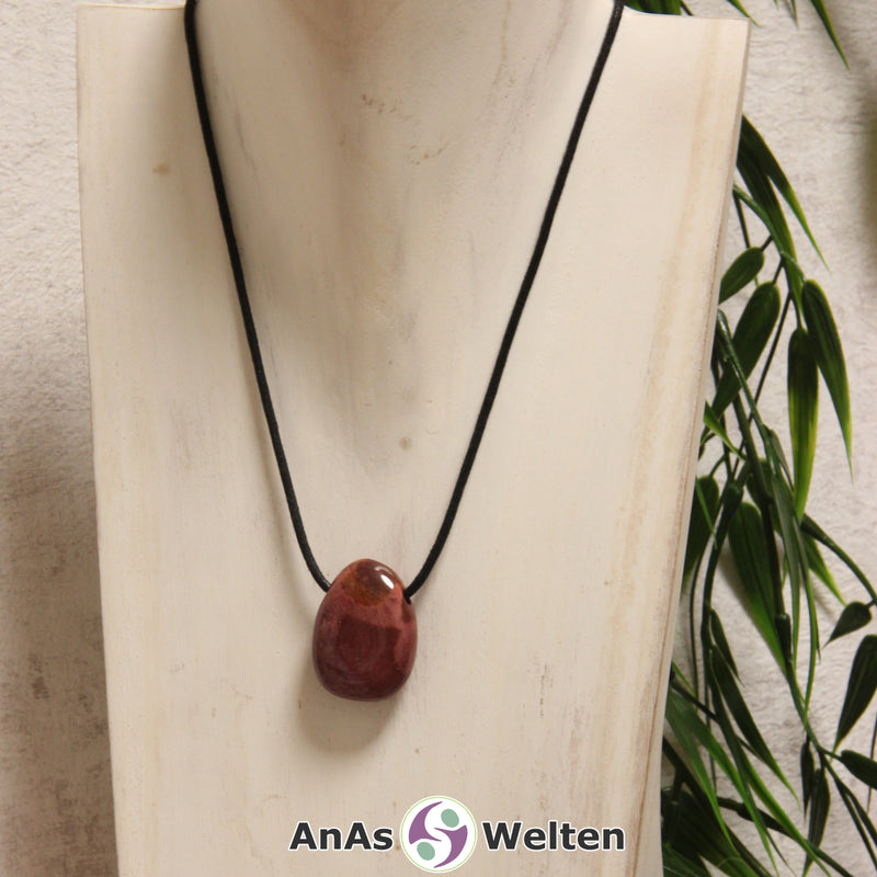 Ein roter Mookait gebohrter Trommelstein an einem schwarzen Baumwollband, der um eine helle Büste gehängt wurde.