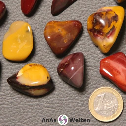 Das Bild zeigt einen Mookait Trommelstein anhand von mehreren Beispielsteinen. Die Edelsteine haben unterschiedliche Farben, sind aber alle einfarbig oder gemischt rot, rotgrau, braun und gelb.