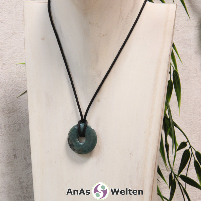 Ein Moosachat Donut als Kette an einem schwarzen gewachsten Baumwollband um eine helle Büste.