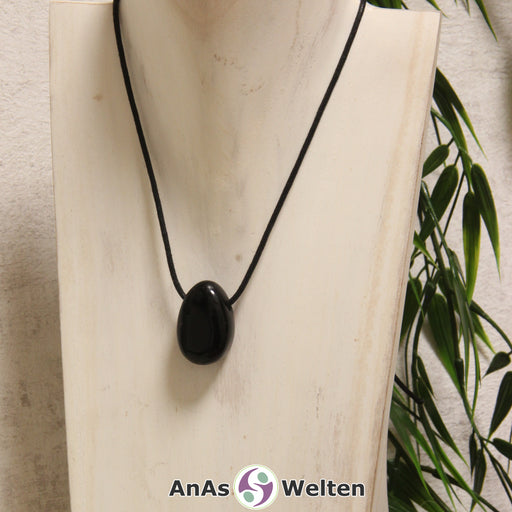 Ein gebohrter Obsidian Trommelstein an einem Baumwollband. Der Edelstein hat eine tiefschwarze Farbe mit einer glänzenden Oberfläche.