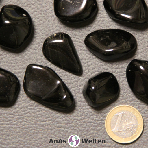 Das Bild zeigt einen Obsidian Trommelstein anhand mehrerer Beispielsteine. Die Edelsteine haben allesamt eine tiefschwarze Farbe, bei einigen sind jedoch kleine Einschlüsse zu erkennen.