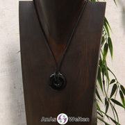 Ein Onyx Donut als Kette an einem schwarzen gewachsten Baumwollband um eine dunkle Büste.