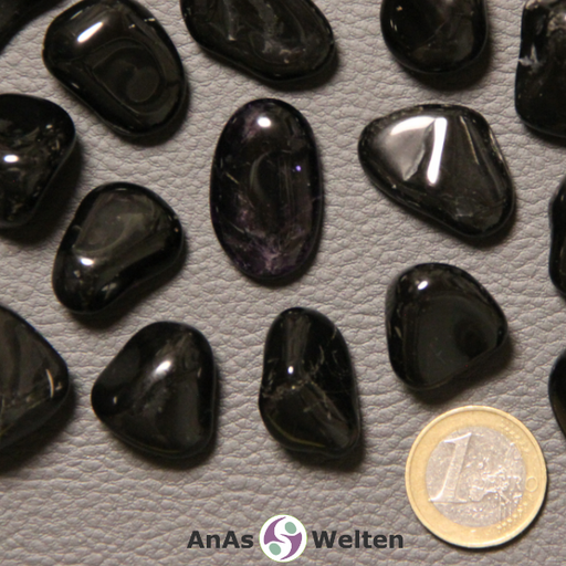 Das Bild zeigt einen Onyx Trommelstein anhand mehrerer Beispielbilder. Die Edelsteine haben allesamt eine tiefschwarze Farbe. Außerdemhaben die meisten von ihnen helle Einschlüsse.