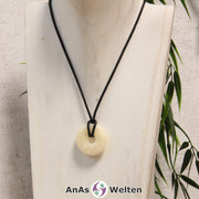 Ein Orangencalcit Donut als Kette an einem schwarzen gewachsten Baumwollband um eine helle Büste.