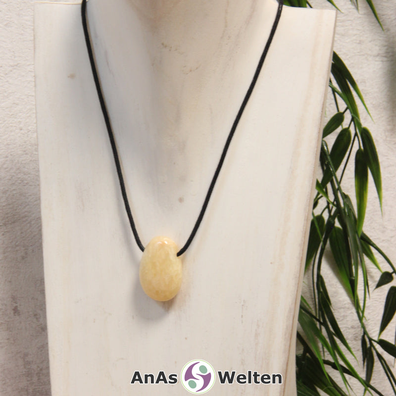Ein gelber Orangencalcit gebohrter Trommelstein an einem schwarzen Baumwollband, der um eine helle Büste gehängt wurde.