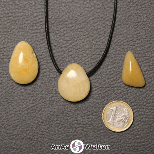 Drei gelbe Orangencalcit gebohrte Trommelsteine nebeneinander. Einer befindet sich an einem schwarzen gewachsten Baumwollband.