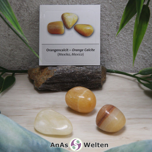 Das Bild zeigt einen Orangencalcit Trommelstein mit Sticker anhand von drei Beispielsteinen. Die Edelsteine haben eine entweder gelbe oder orangene Farbe. Außerdem haben zwei von ihnen weiße Risse in ihrem Inneren und der eine einen braunen Streifen.