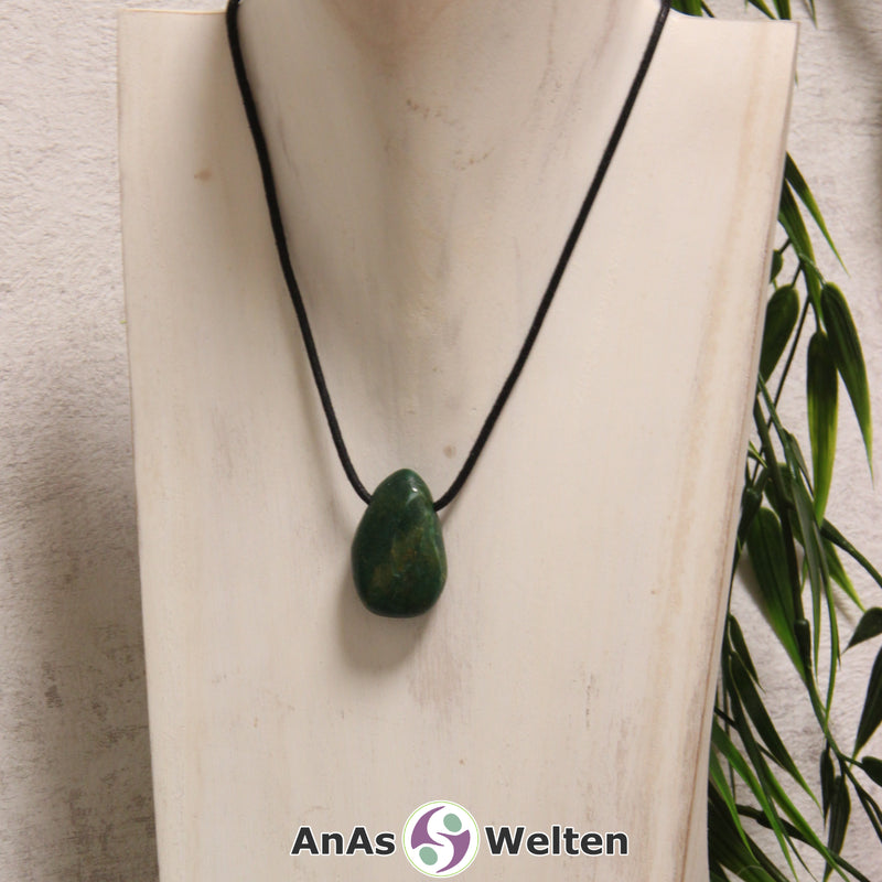 Ein grüner Prasem gebohrter Trommelstein an einem schwarzen Baumwollband, der um eine helle Büste gehängt wurde.