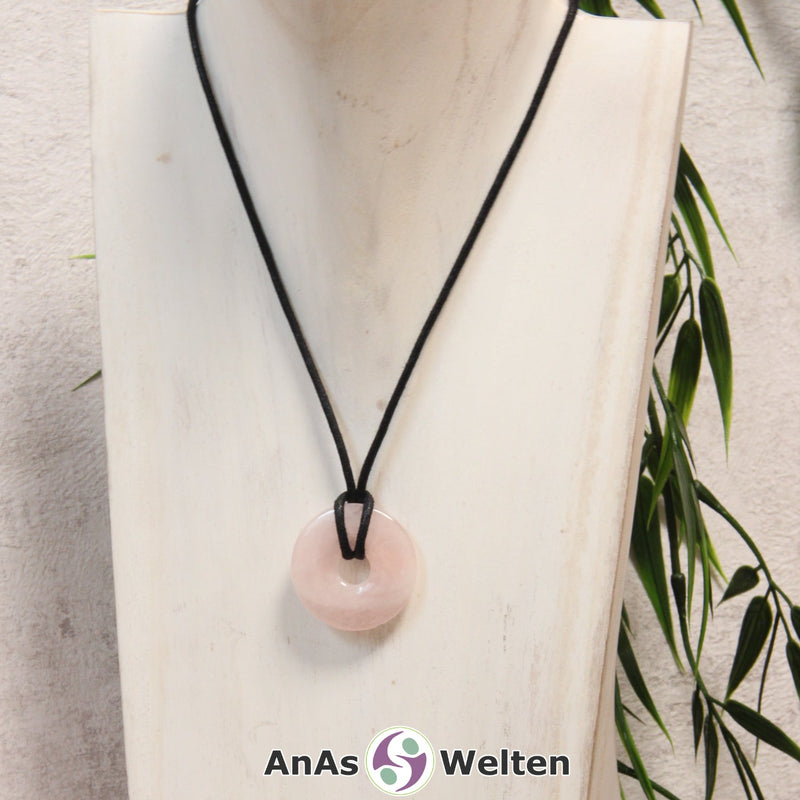 Ein Rosenquarz Donut als Kette an einem schwarzen gewachsten Baumwollband um eine helle Büste.