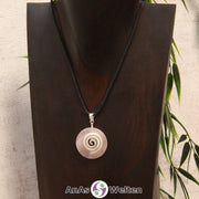 Ein Rosenquarz Donut an einem Donut-Halter Spirale, der mit einem gewachsten Baumwollband um eine dunkle Büste hängt.