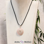 Ein Rosenquarz Donut an einem Donut-Halter Spirale, der mit einem gewachsten Baumwollband um eine helle Büste hängt.