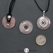 Drei Rosenquarz Donuts nebeneinander. Einer an einem Baumwollband, ein anderer an einem Donut-Halter mit Baumwollband.