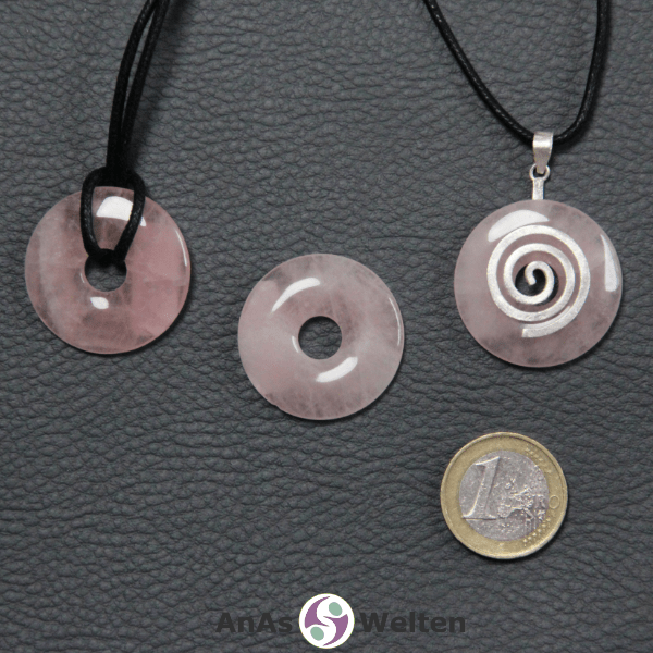 Drei Rosenquarz Donuts nebeneinander. Einer an einem Baumwollband, ein anderer an einem Donut-Halter mit Baumwollband.