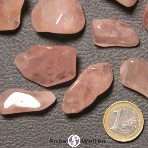 Das Bild zeigt einen Rosenquarz Trommelstein anhand mehrerer Beispielsteine. Die Edelsteine haben eine rosa Farbe und sind halbtransparent. In ihrem Inneren kann man die typischen hellen Risse erkennen.