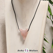 Ein Rosenquarz Wolf Anhänger an einem schwarzen Baumwollband, der um eine dunkle Büste gehängt wurde.