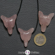 Drei Rosenquarz Wolf Anhänger nebeneinander. Einer befindet sich an einem schwarzen Baumwollband.