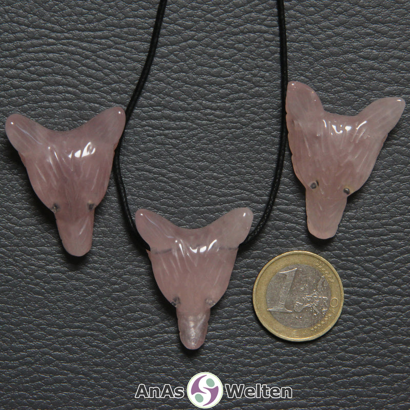 Drei Rosenquarz Wolf Anhänger nebeneinander. Einer befindet sich an einem schwarzen Baumwollband.