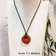 Ein Roter Jaspis Donut als Kette an einem schwarzen gewachsten Baumwollband um eine helle Büste.