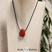 Ein Roter Jaspis gebohrter Trommelstein an einem schwarzen Baumwollband, der um eine helle Büste gehängt wurde.