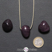 Drei lila-rote Rubin gebohrte Trommelsteine nebeneinander. Einer befindet sich an einem beigen gewachsten Baumwollband.