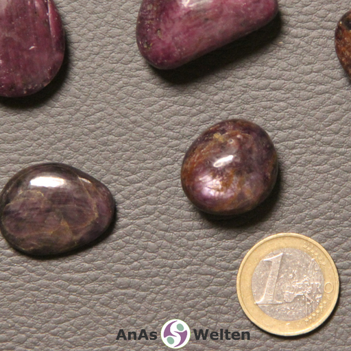 Das Bild zeigt einen Rubin Trommelstein anhand mehrerer Beispielsteine. Die Edelsteine haben eine dunkelrot-lila Farbe mit mehreren hellen Einschlüssen.