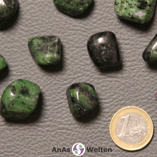 Das Bild zeigt einen Rubin Zoisit Trommelstein anhand mehrerer Beispielsteine. Die Edelsteine sind hauptsächlich grün und schwarz und haben kleine rote Einschlüsse.