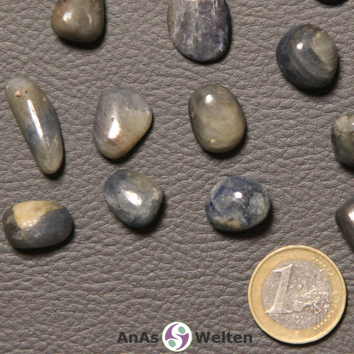 Das Bild zeigt einen Saphir Trommelstein anhand mehrerer Beispielsteine. Die Edelsteine haben hellblaue, dunkelblaue und graublaue Farben. Außerdem haben sie gelegentliche braungraue Einschlüsse.