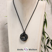 Ein Schneeflocken-Obsidian Donut als Kette an einem schwarzen gewachsten Baumwollband um eine helle Büste.