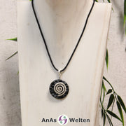 Ein Schneeflocken-Obsidian Donut an einem Donut-Halter Spirale, der mit einem gewachsten Baumwollband um eine helle Büste hängt.