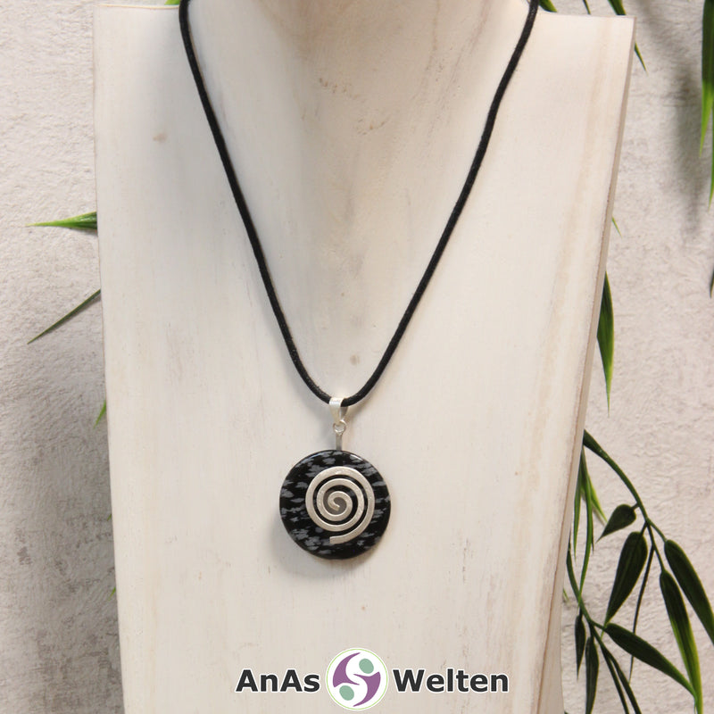 Ein Schneeflocken-Obsidian Donut an einem Donut-Halter Spirale, der mit einem gewachsten Baumwollband um eine helle Büste hängt.