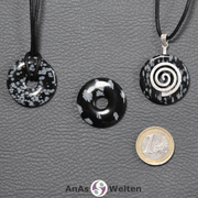 Drei Schneeflocken-Obsidian Donuts nebeneinander. Einer an einem Baumwollband, ein anderer an einem Donut-Halter mit Baumwollband.