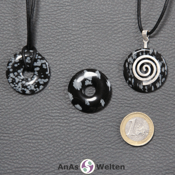 Drei Schneeflocken-Obsidian Donuts nebeneinander. Einer an einem Baumwollband, ein anderer an einem Donut-Halter mit Baumwollband.