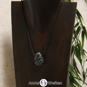 Ein schwarz-weiße Schneeflocken-Obsidian gebohrter Trommelstein an einem schwarzen Baumwollband, der um eine dunkle Büste gehängt wurde.