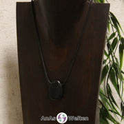 Ein schwarzer Schungit gebohrter Trommelstein an einem schwarzen Baumwollband, der um eine dunkle Büste gehängt wurde.