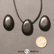 Drei schwarze Schungit gebohrte Trommelsteine nebeneinander. Einer befindet sich an einem schwarzen gewachsten Baumwollband.