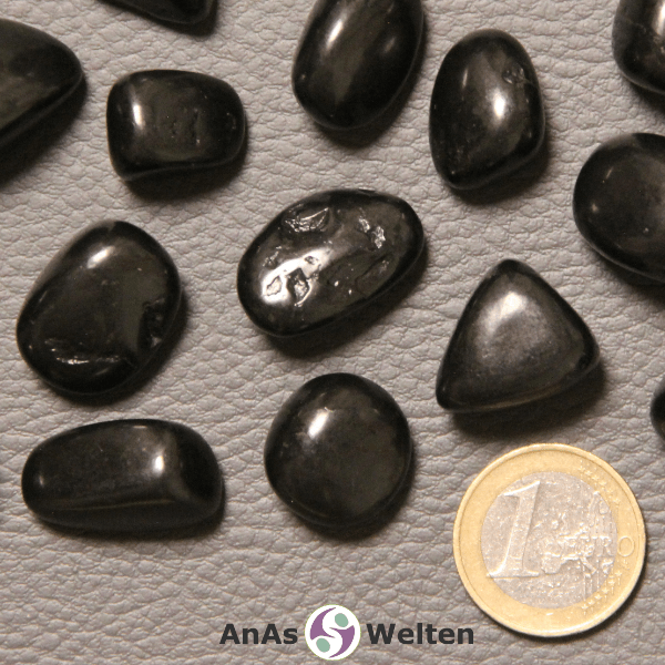 Das Bild zeigt einen Schungit 	Trommelstein anhand mehrerer Beispielsteine. Die Edelsteine haben alle eine schwarze Farbe und die meisten von ihnen einen leicht matten Glanz.