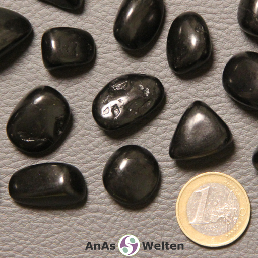 Das Bild zeigt einen Schungit 	Trommelstein anhand mehrerer Beispielsteine. Die Edelsteine haben alle eine schwarze Farbe und die meisten von ihnen einen leicht matten Glanz.