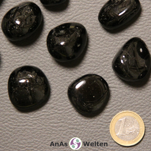 Auf dem Bild ist ein schwarzer Turmalin (Schörl) Trommelstein anhand mehrerer Beispielsteine zu sehen. Die Edelsteine haben allesamt eine schwarze Grundfarbe mit gelegentlichen Einschlüssen. Die geschliffene Oberfläche weißt bei einigen Steinen Unebenheiten auf.